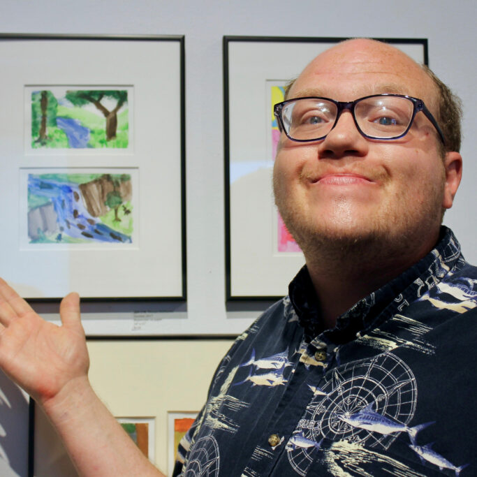 Tom smiles and points to his artwork in CATA's 2018 Annual Art Show
