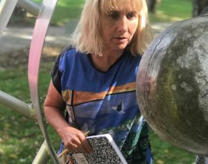 A woman holds a pencil and notebook while looking at a large, metal ball