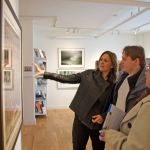 Three people look and talk about a large framed photo in an art gallery