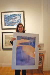 A woman smiles and holds a large photograph of sand dunes