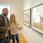 A man and woman smile while looking at a large framed photograph of a lion
