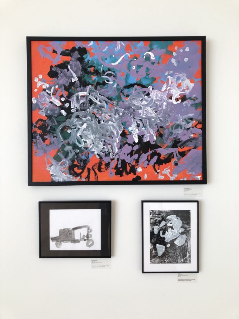 Three paintings on a wall: one large and colorful, two small black and white paintings beneath it.