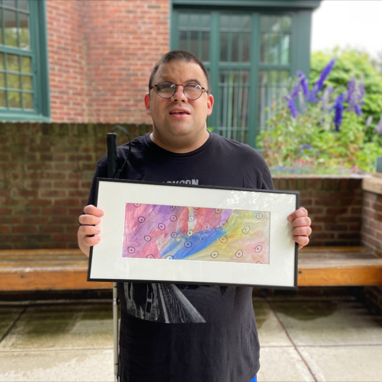 Image description: Anthony standing holding a framed painting.