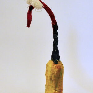 Mixed media bottle sculpture creature with a yellow base, two legs-one red and one blue, a long neck that starts navy and becomes red towards a curved head. A mop of yellow string creates the appearance of hair.