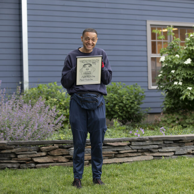Franck stands outside smiling and holding a small framed drawing