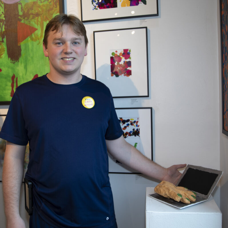 Andrew stands in a gallery pointing to a scupture in CATA's 2019 Annual Art Show