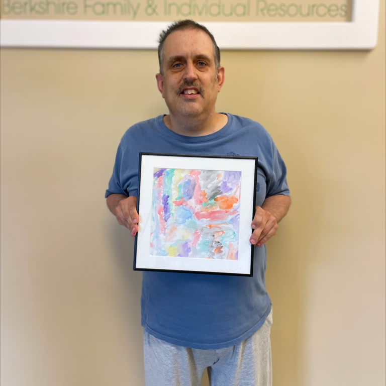 Image description: Brent smiles and holds his framed painting