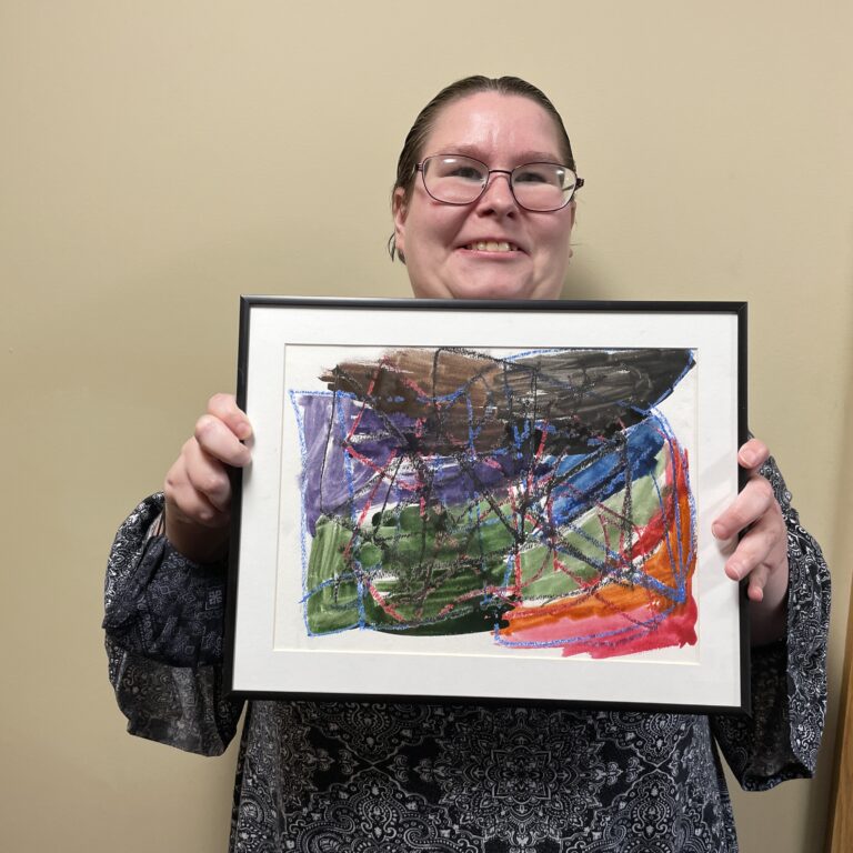 Catie stands and smiles while holding her framed painting