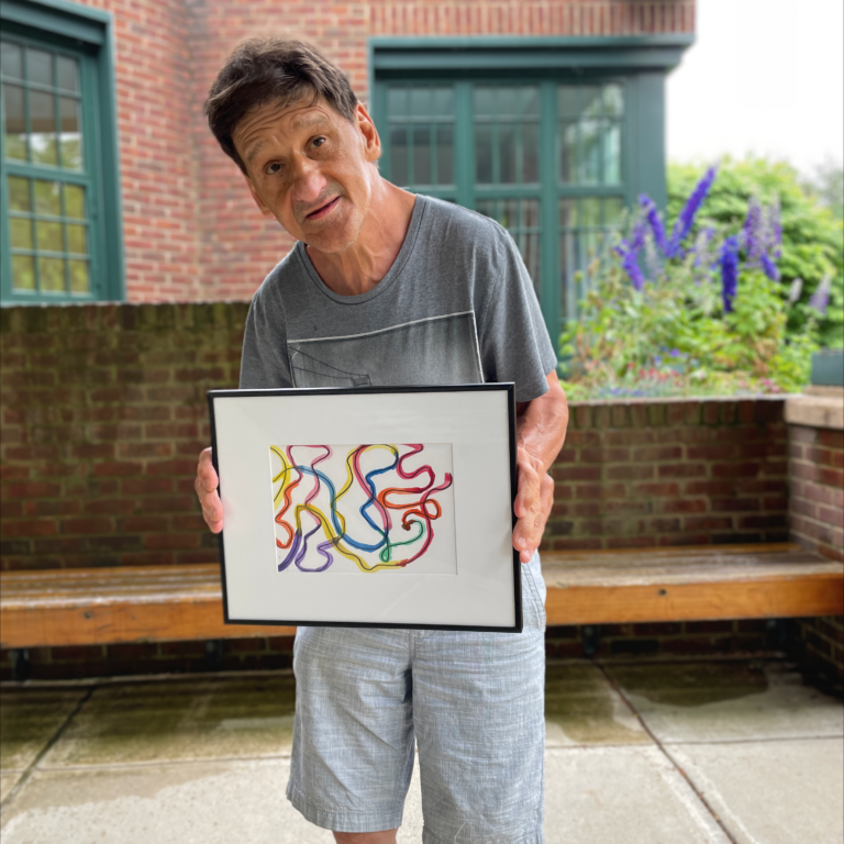Image description: Dennis stands outside holding his framed painting