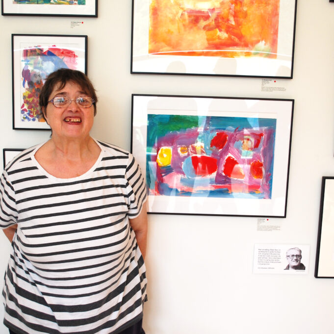 Image description: Diane smiles in front of her painting on the wall of the Clark Art Institute during CATA's 2018 Annual Art Show