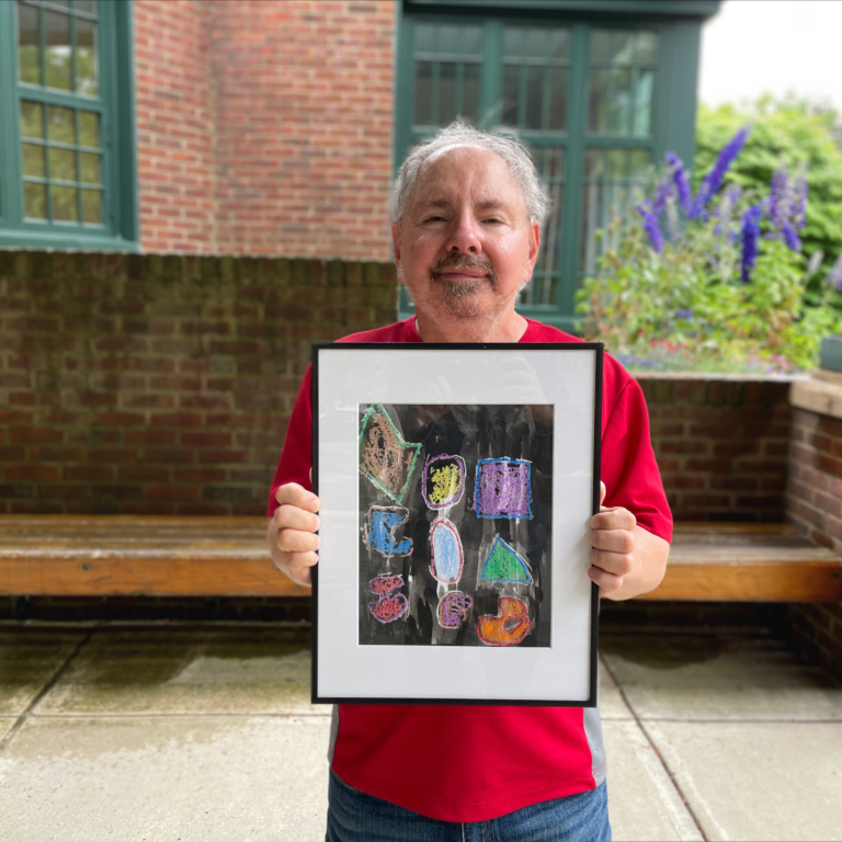 Doug stands outside in a red shirt holding his framed painting