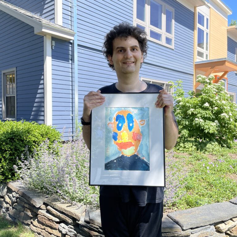 A man stands outside and holds a framed painting