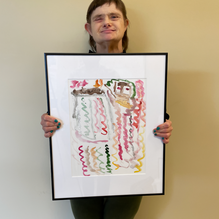 Image Description: Janet standing against a beige background holding her framed painting