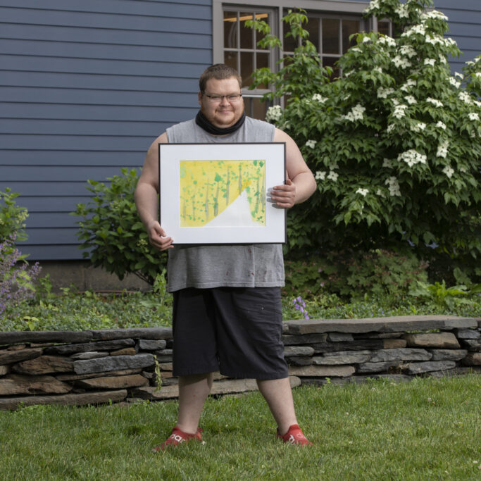 Image description: Justin stands outside smiling and holding his framed painting