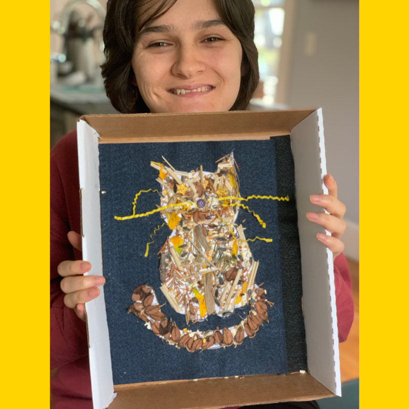 Kelsey smiles and holds a multimedia artwork of a cat, built inside a box