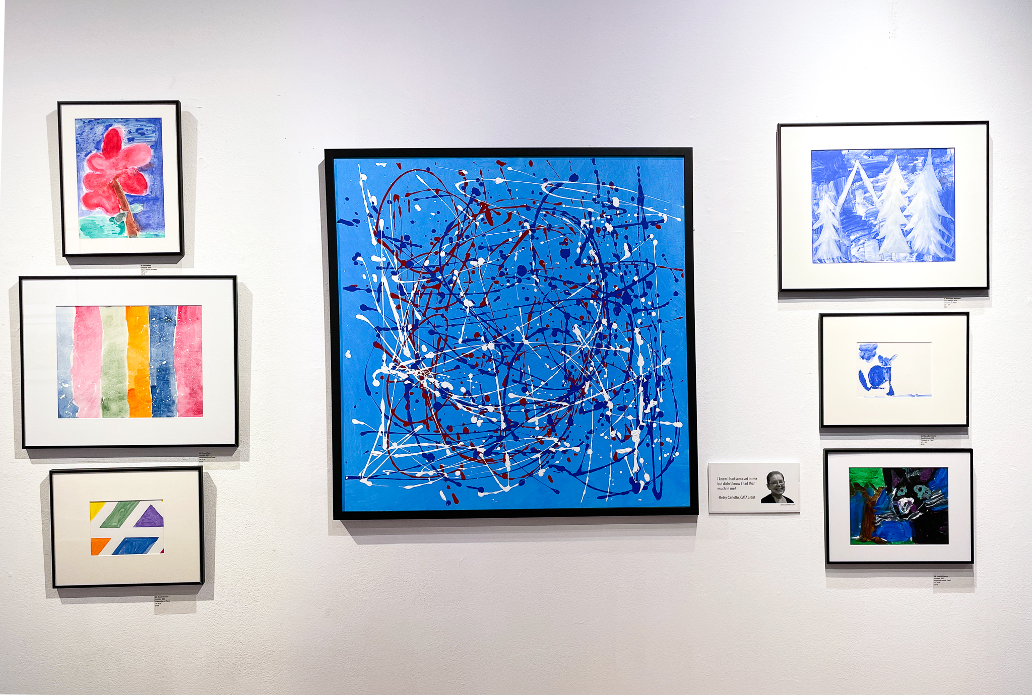 Gallery wall with an assortment of small abstract paintings and one large blue painting in the center