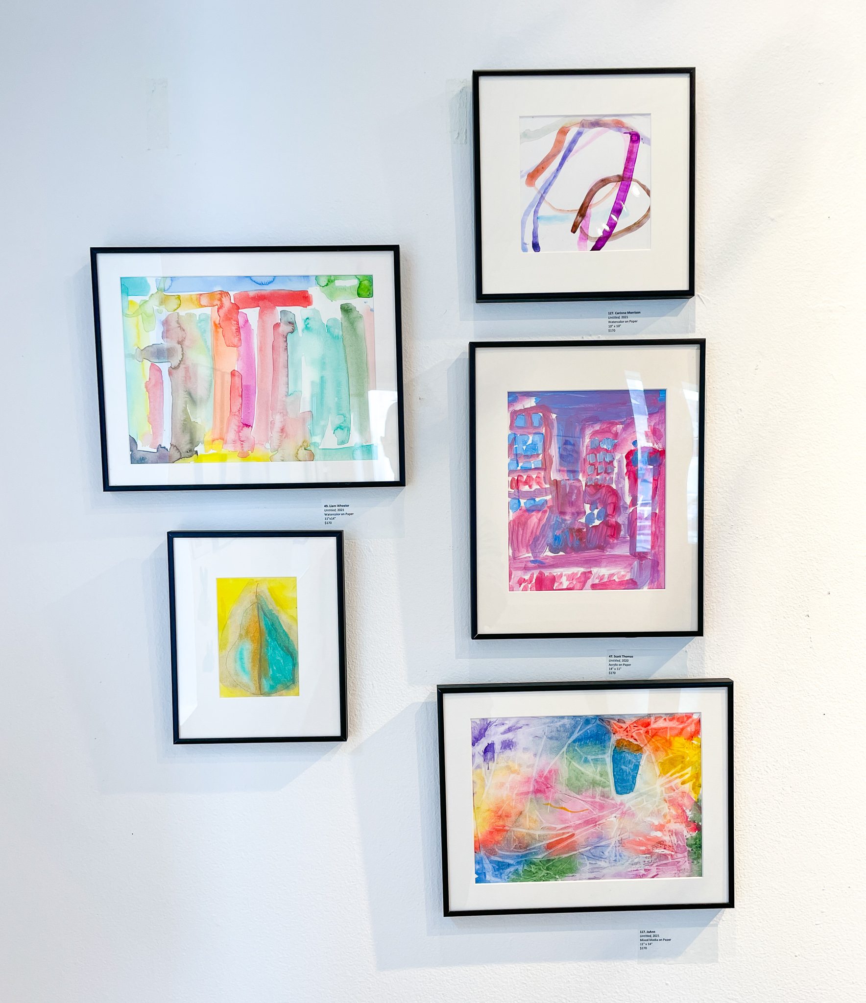 Gallery wall with five multicolored abstract paintings in black frames