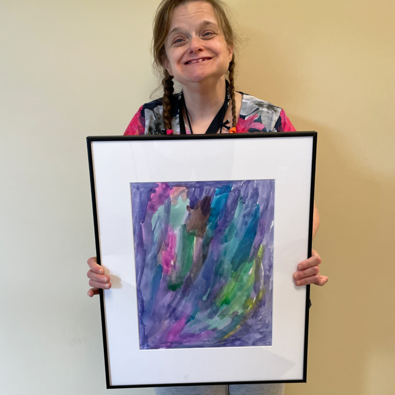 Lisa stands smiling and holding a large framed painting