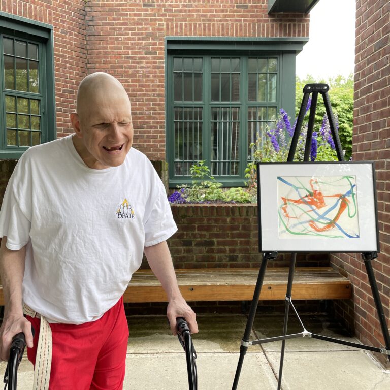 Image description: Michael stands with a walker next to his framed artwork on an easel