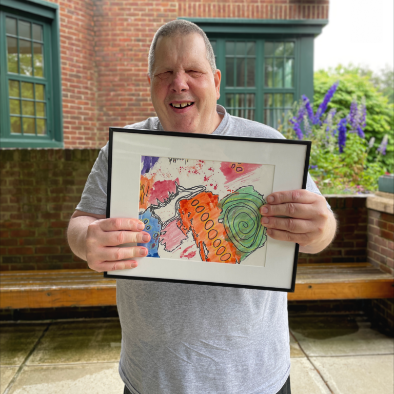 Richard stands outside smiling and holding his framed painting