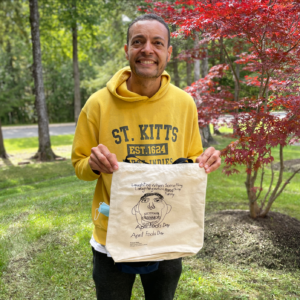 Artist Franck Felix smiling and holding a tote bag with his artwork on it