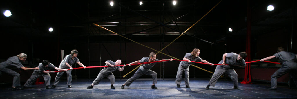 A line of CATA dancers in jumpsuits hold a red rope