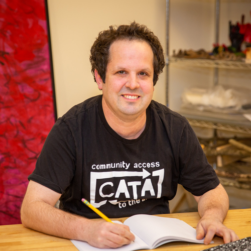CATA writer Scott Thomas smiles while writing in a notebook