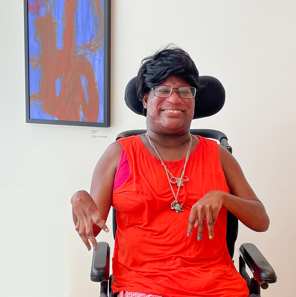 An artist in a wheelchair smiles next to an abstract painting