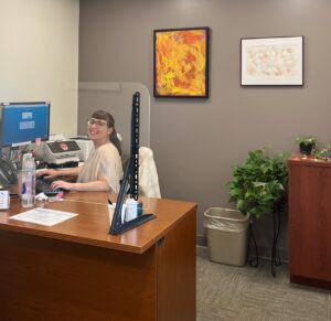 An employee at Greylock smiling at her desk. On the wall is a painting by a CATA artist.