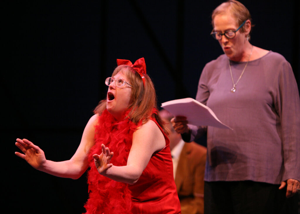 Teresa acting on stage in a red costume and feather boa.