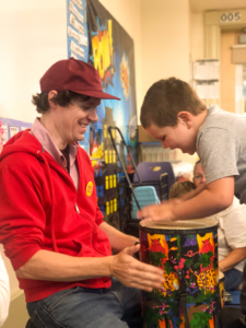 A CATA faculty artist on the left holds a drum while a young student plays.