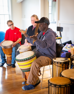 Bolokada Conde leads a drumming workshop in the CATA studio. Beside him is a CATA artist and CATA faculty artist who watch him play.