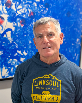 David Rosenthal smiles and stands in front of a blue abstract painting.