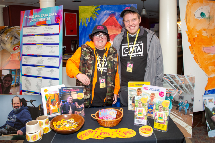 CATA artists Izzy and Kyle smile next to a table with CATA materials and swag