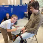 A young boy smiles and plays a drum