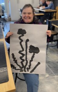 Sarah Vannah smiles while holding her flower painting that was curated for the exhibit.