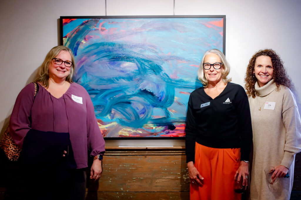 Photo: Staff from Acrisure, who sponsored the exhibit, pose with a painting by Katrina Couture— which they purchased for the Acrisure conference room!