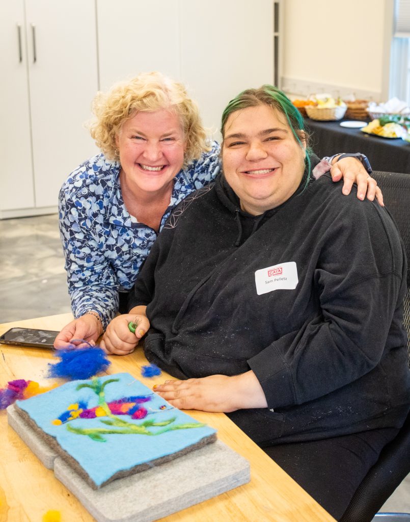 Heather Wells Heim, President of CATA's Board of Directors, poses with CATA artist Sam Pelletz while working on an underwater scene.