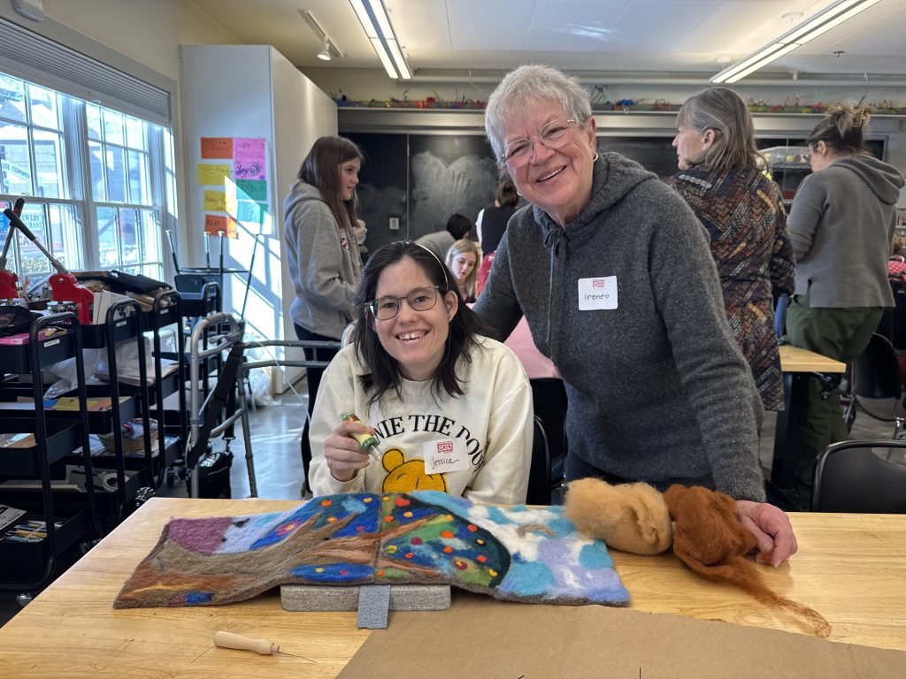 Irene poses with CATA artist Jessica as she begins to combine two felt panels of a colorful tree.