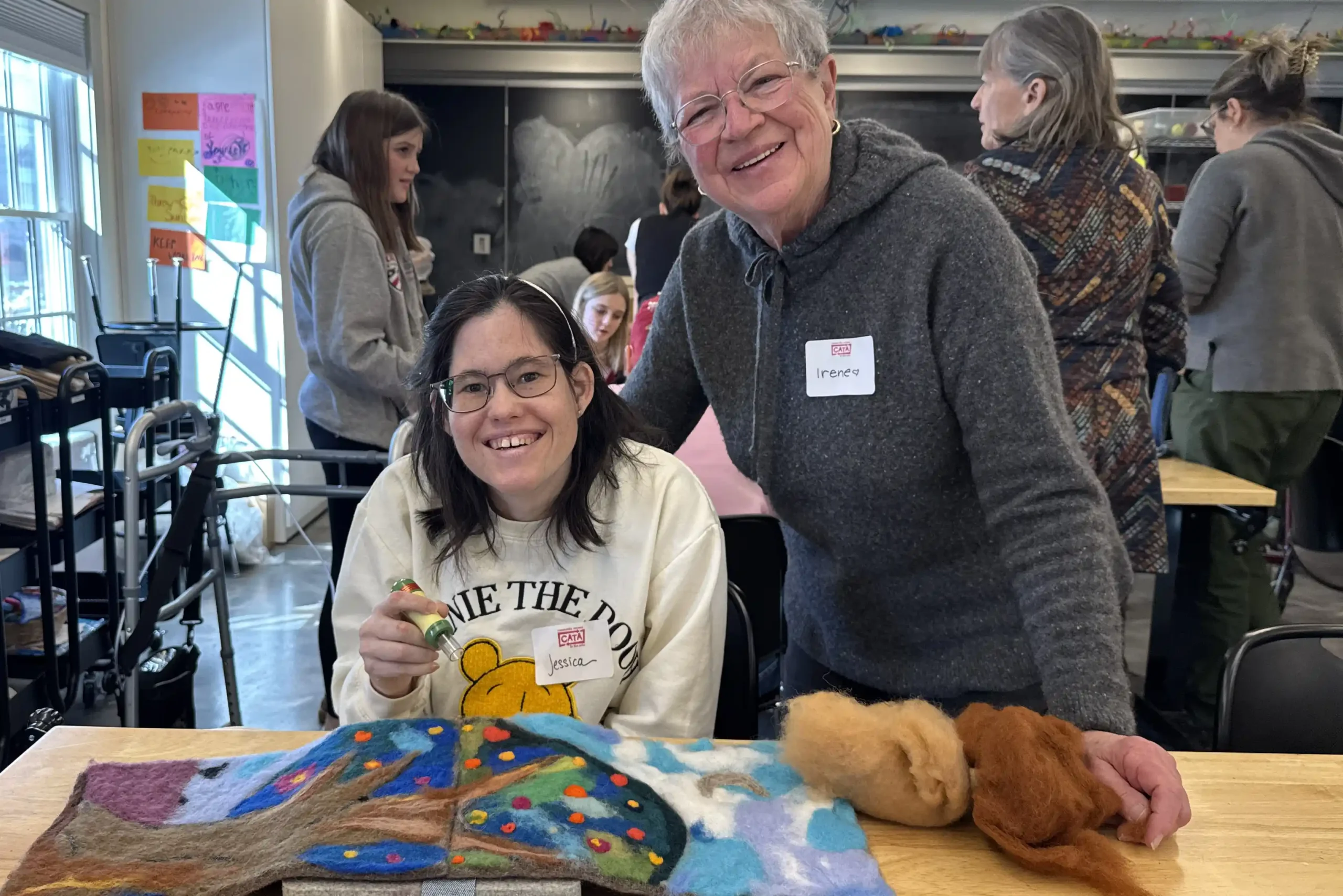 Jessica and Irene work on joining two felt panels to create a colorful tree.
