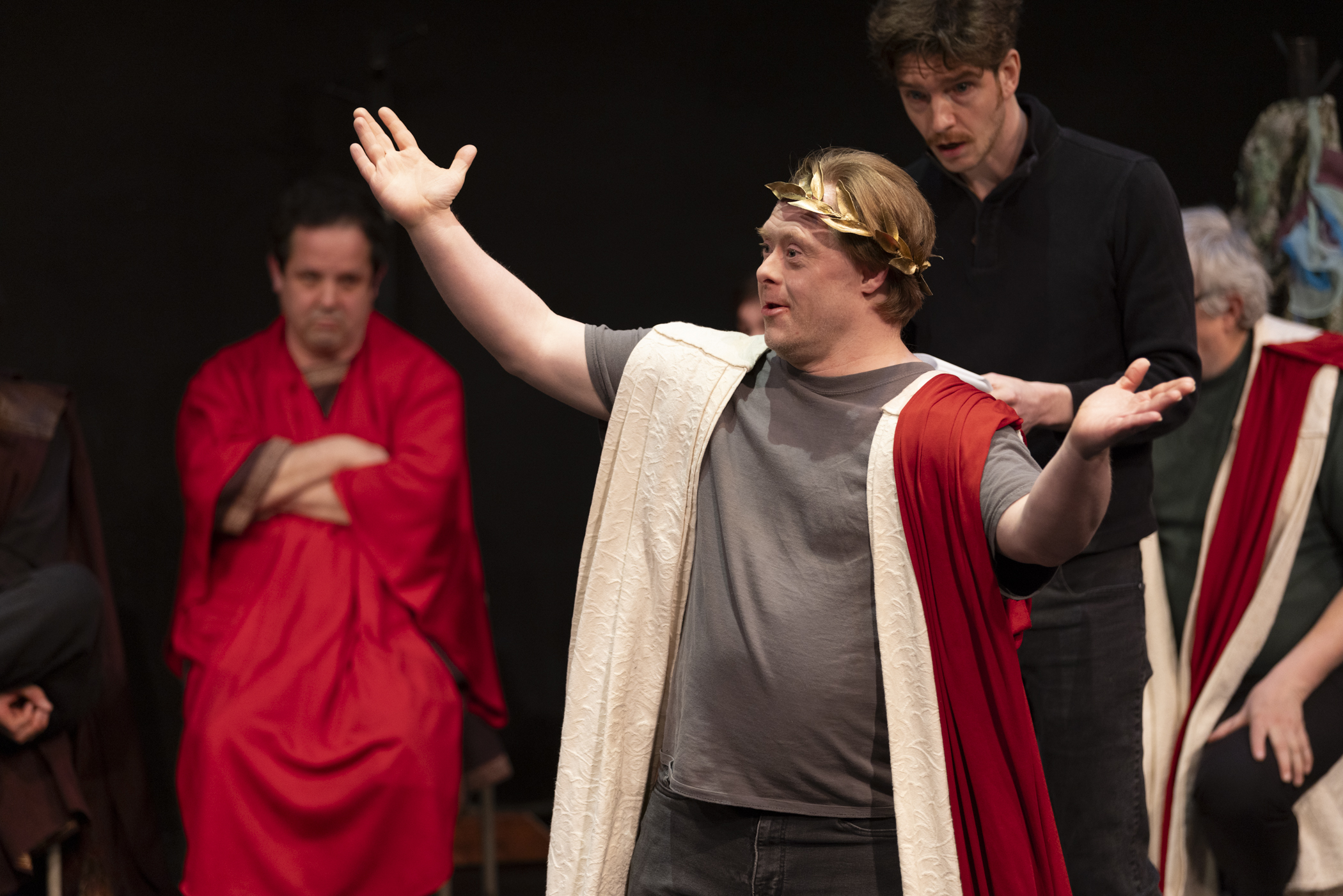 As Caesar, Dan lifts his hands above his head.