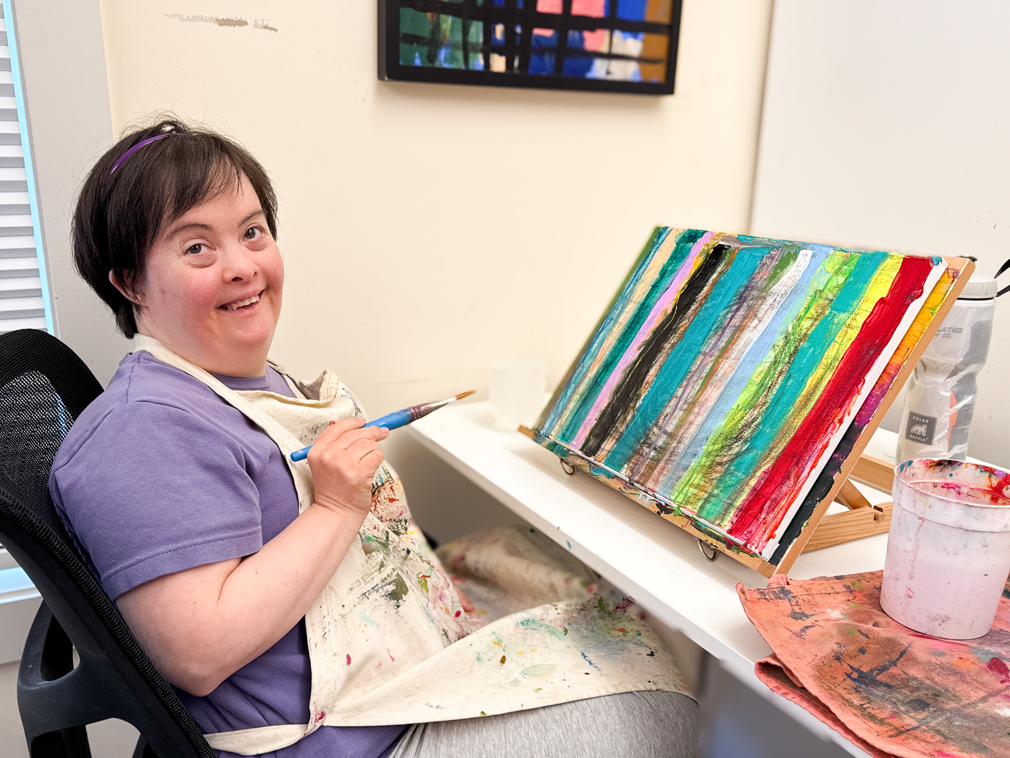 An artist sits in front of a canvas with a paintbrush.