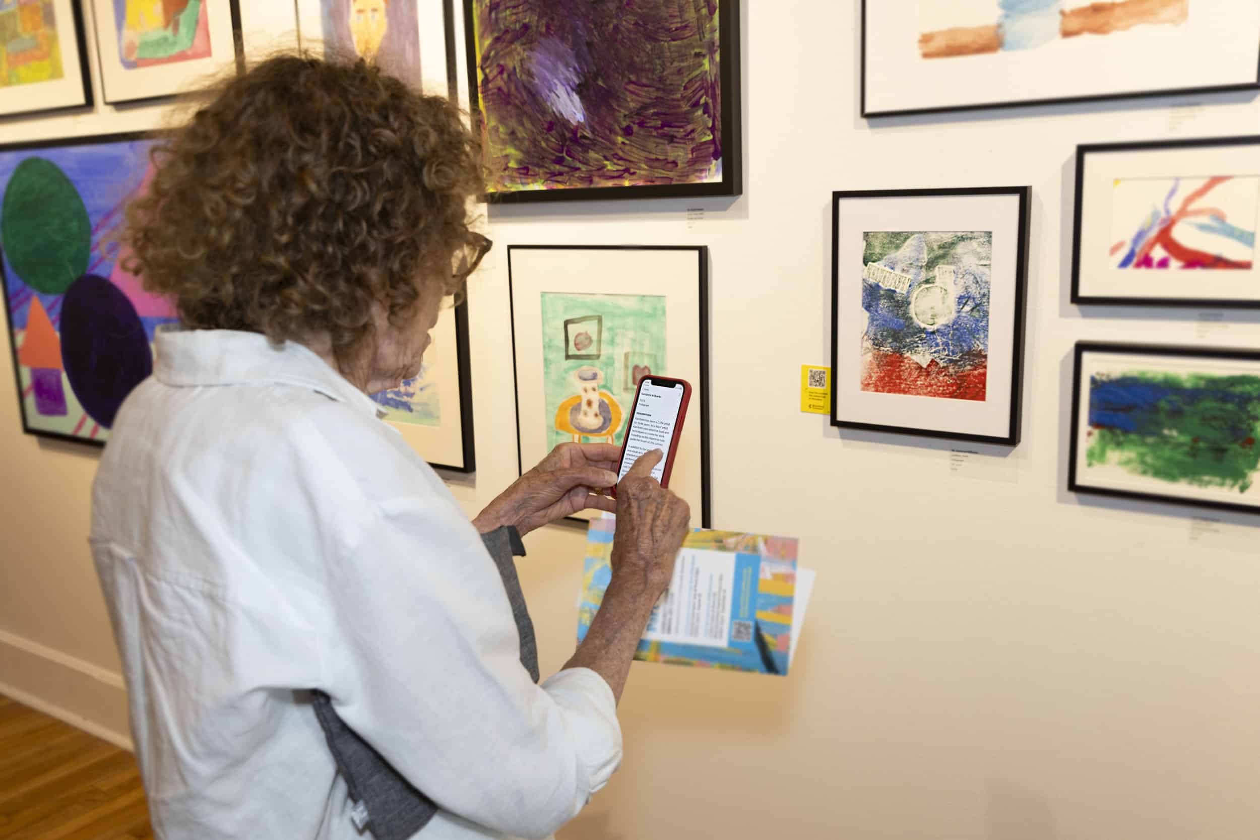 A woman scans a QR code near artwork.