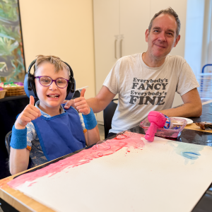 A father and son sit in front of an art project.