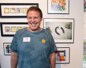 An artist smiles with his work at an exhibit.
