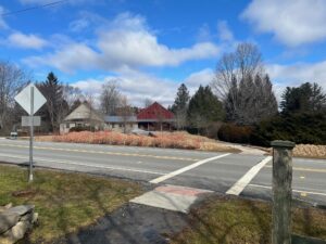 Image description: A gravel pathway leads to a crosswalk. Across the street is the Center House at Berkshire Botanical Garden.