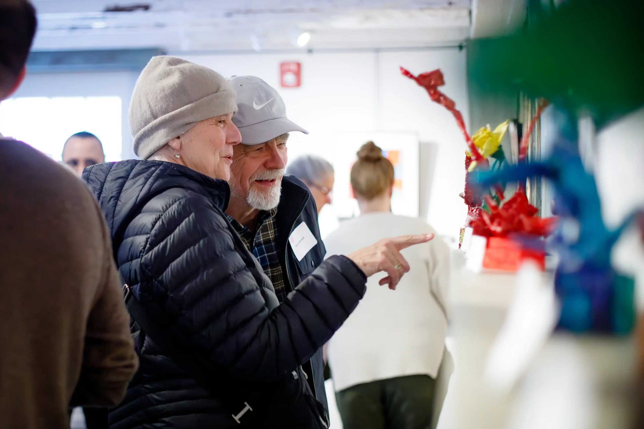 Two people examine a lineup of floral sculptures on the mantle.