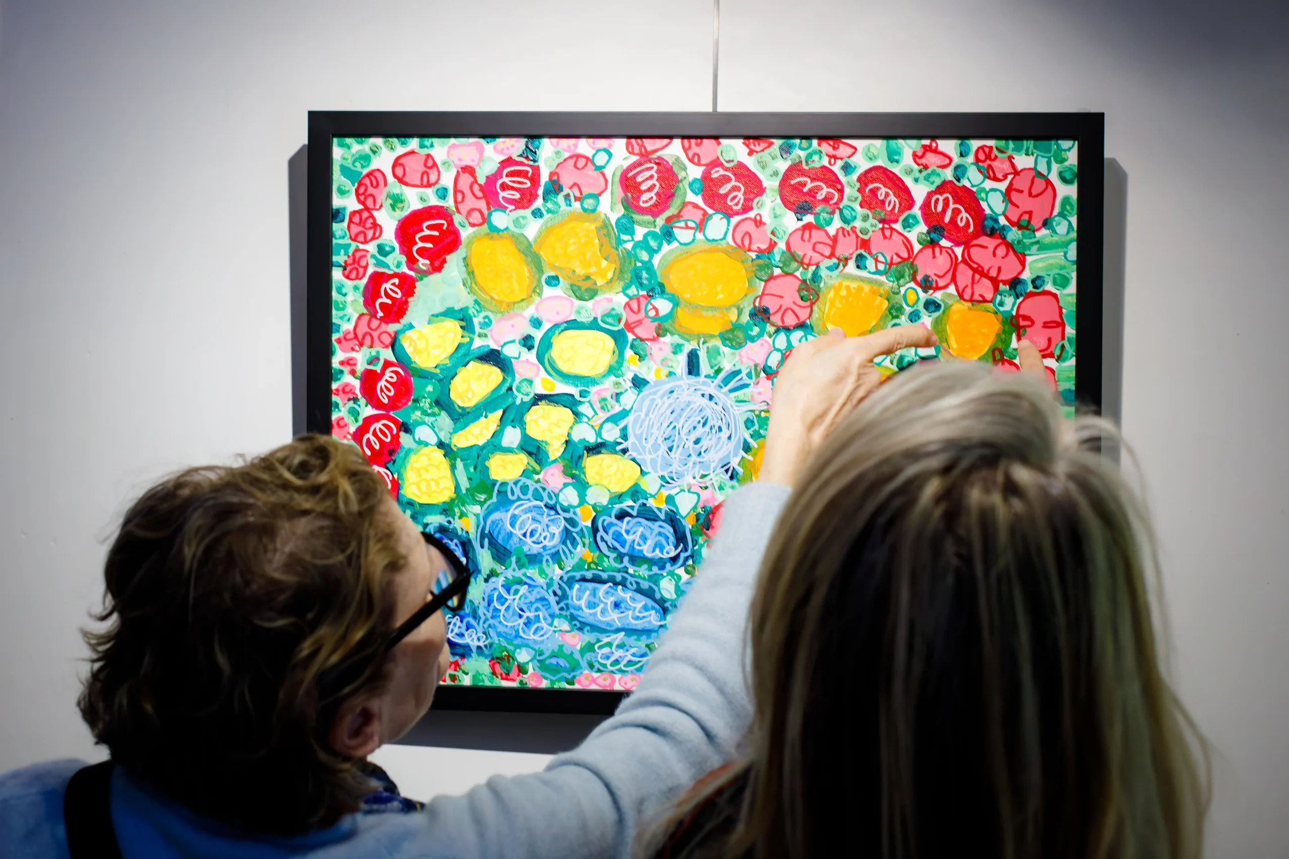Two women discuss the arc of flowers in Sandra Caicedo's painting, "Pink."