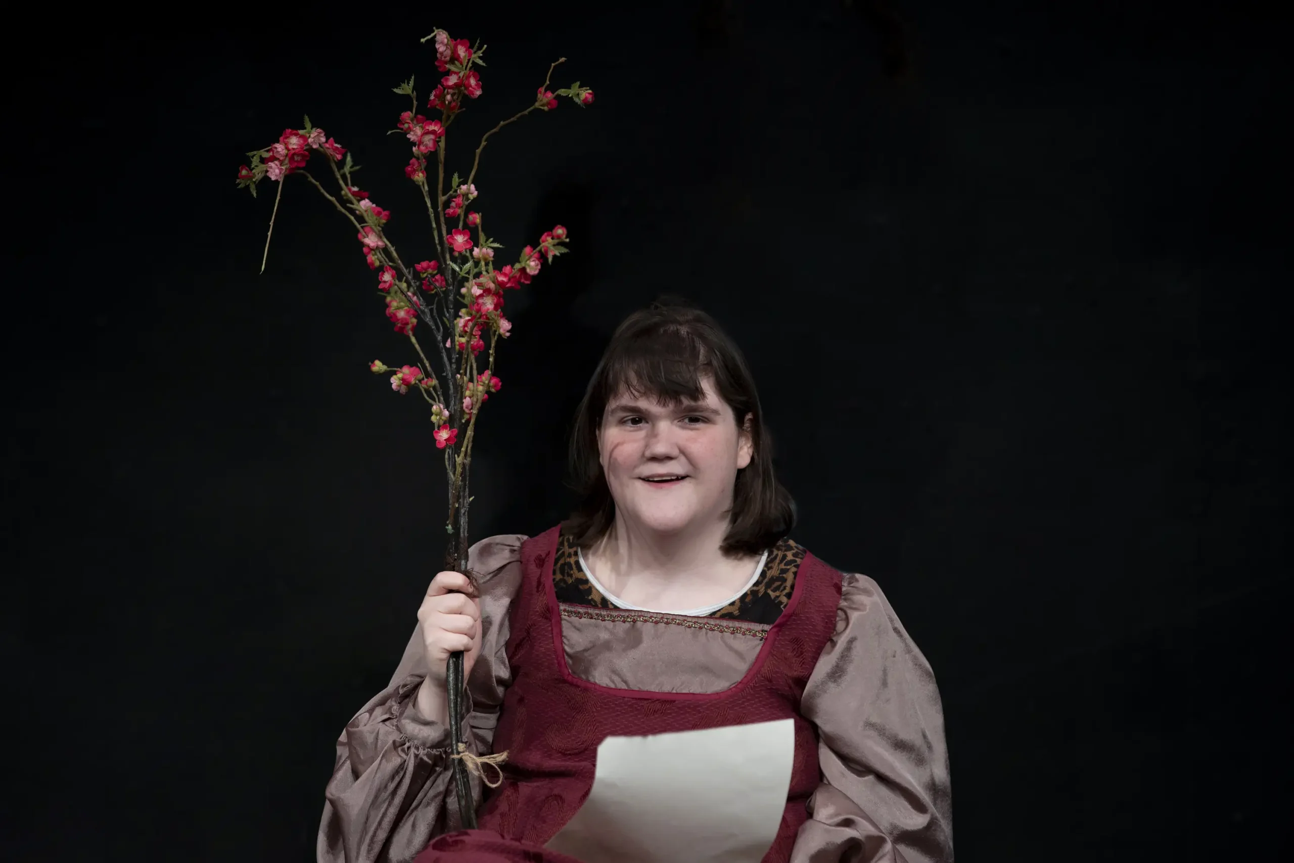 Keira delivers a message from behind a branch of flowers.
