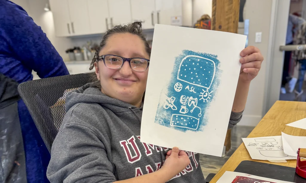 CATA artist Lahna holds a blue printed painting.